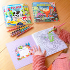 Coloring books and crayons on a wooden table with a child coloring.