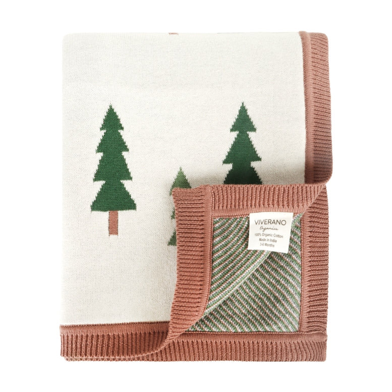 A folded knit baby blanket by Viverano, featuring a cream-colored front with green pine tree motifs and a dusty rose pink ribbed border. The underside is shown folded over, revealing a striped pattern in sage green and cream, with a white brand label sewn onto the corner.