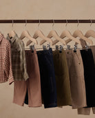 A clothing rack displaying multiple pairs of shorts in different colors and patterns, including pink, navy, olive green, beige, and black, hanging on wooden hangers against a warm beige background.