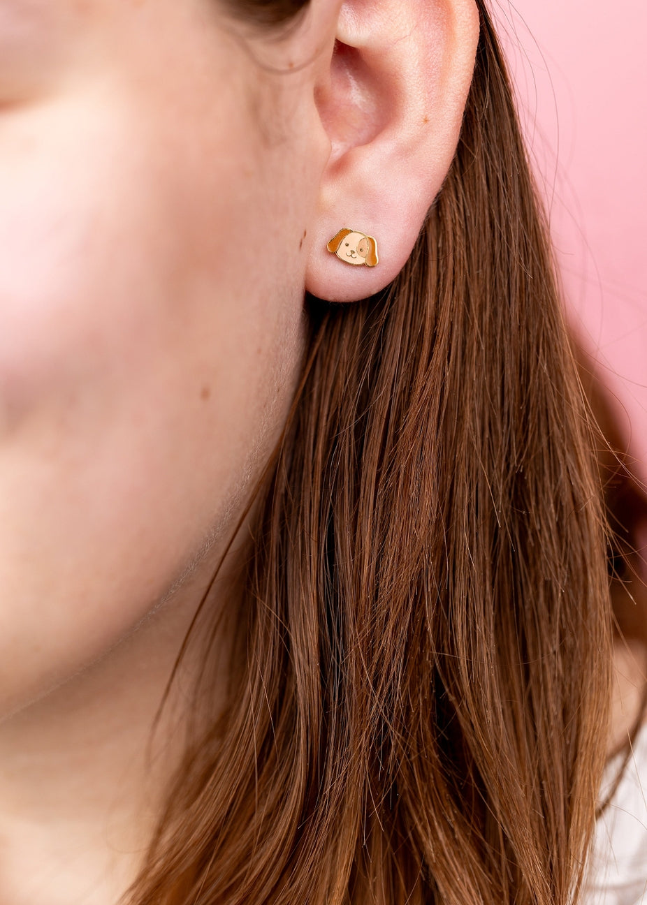 Close-up of an ear wearing a gold earring with a small heart design.