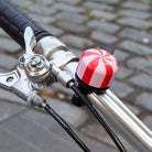 Close-up of a bicycle handlebar with a red and white striped bell on a blurred pavement background