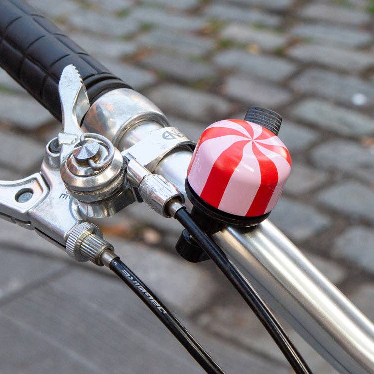 Close-up of a bicycle handlebar with a red and white striped bell on a blurred pavement background