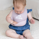 Baby wearing a bib with 'Lil Bestie' text sitting on a light-colored surface.