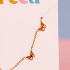 Butterfly-shaped earrings on a gold chain against a colorful background