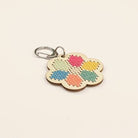 Flower-shaped keychain with colorful embroidered design on a beige background