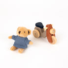 Small teddy bear in a blue dress next to a wooden toy vehicle on a white background