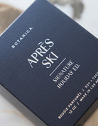 A close-up of a Botanica After Ski Signature Holiday Ed. perfume box, featuring a dark navy blue textured surface with elegant white typography.