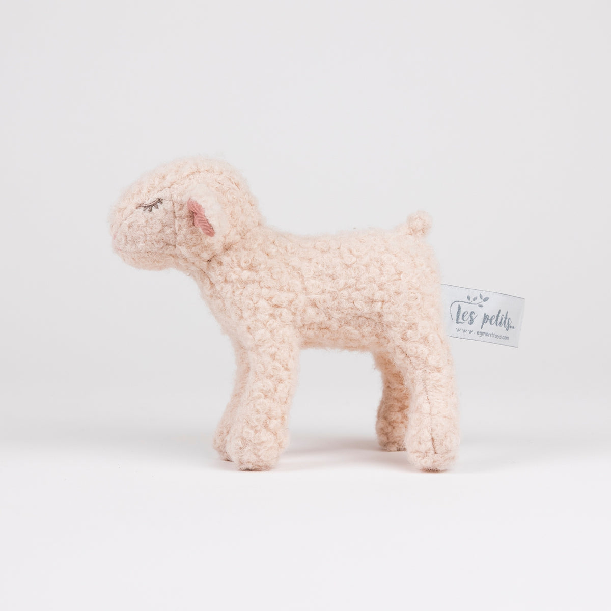A small plush sheep toy in a soft cream bouclé fabric, standing on a seamless white studio background. A small paper brand tag reading 'Les petits.