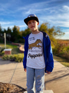 A boy wearing an off-white short-sleeve t-shirt with blue jacket, featuring a graphic of a running puppy with the text 'BRING ME ALL THE Puppies'