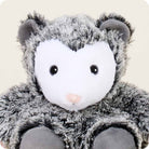 A close-up view of the Opossum by Warmies stuffed animal, highlighting its white face, round black button eyes, pink nose, and fluffy gray-and-black textured fur.