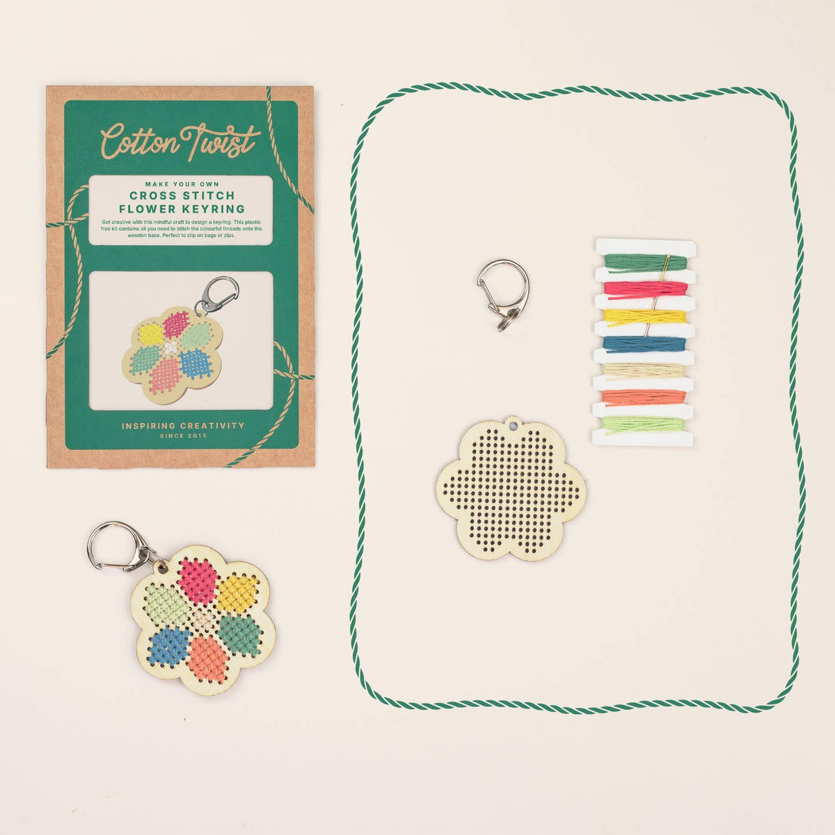 Cross stitch flower keyring kit with packaging, keyring, and thread on a beige background