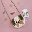 Fluffy dog-shaped purse with decorative hair clips on a pink background