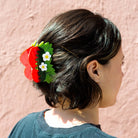 Person with a decorative hair clip resembling strawberries and flowers against a pink background