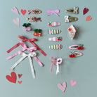 Collection of colorful hair accessories including bows and heart shapes on a light blue background.