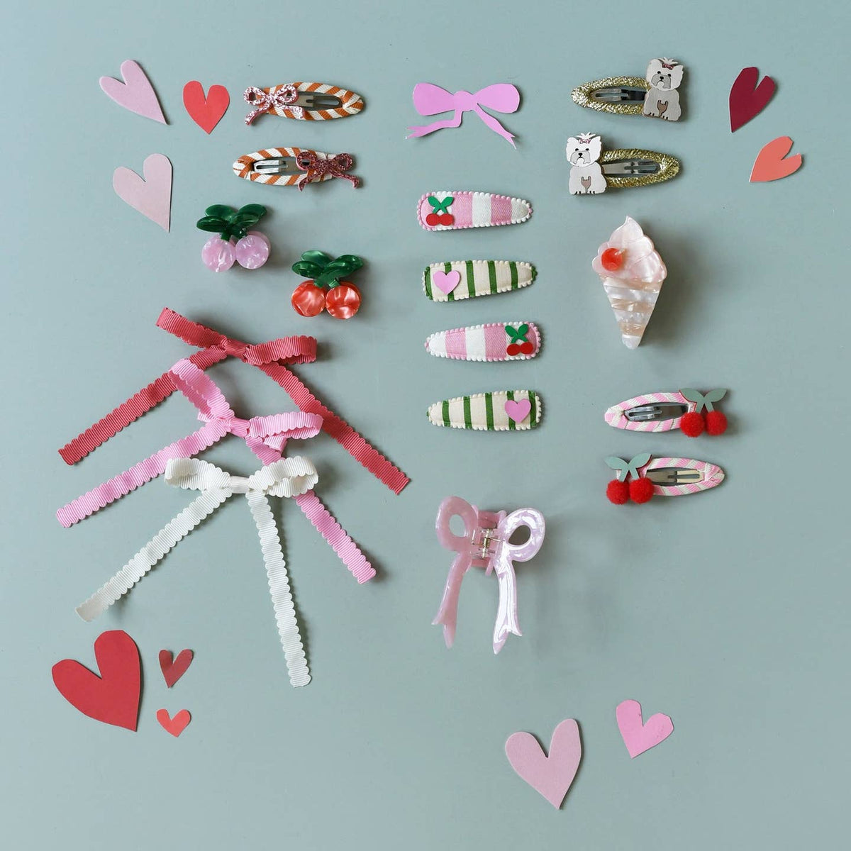 Collection of colorful hair accessories including bows and heart shapes on a light blue background.