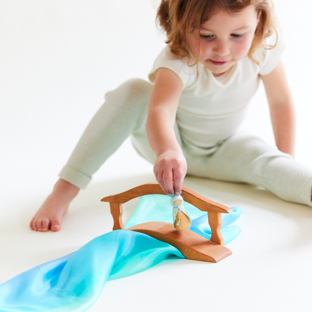 Child playing with a toy mermaid on a white surface