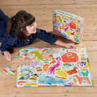 Child playing with a colorful puzzle on a wooden floor next to the puzzle box.