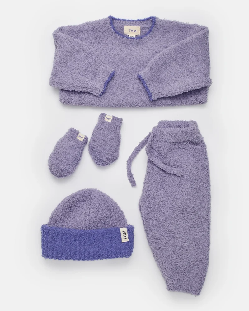 A complete taro purple fuzzy winter set arranged flat against a white background, featuring a boxy sweater, lounge pants with a drawstring, a beanie hat, and mittens.