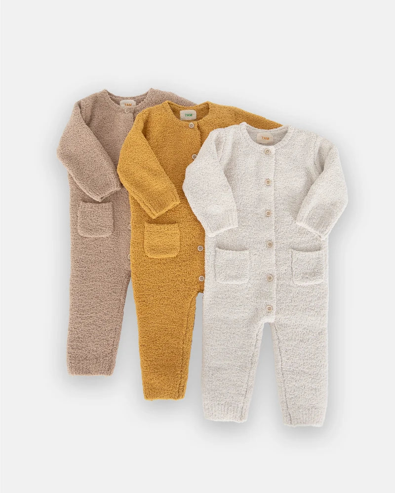 Three long-sleeve fuzzy rompers by 7AM Enfant in taupe, mustard yellow, and ecru laid flat in a row on a white background.