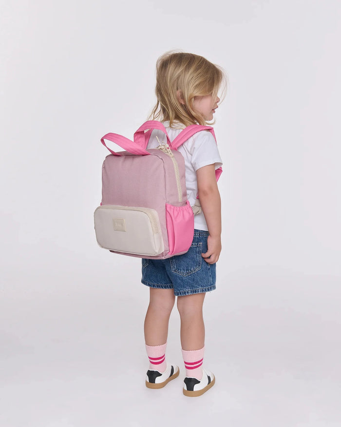 Child wearing a pink and beige backpack on a white background