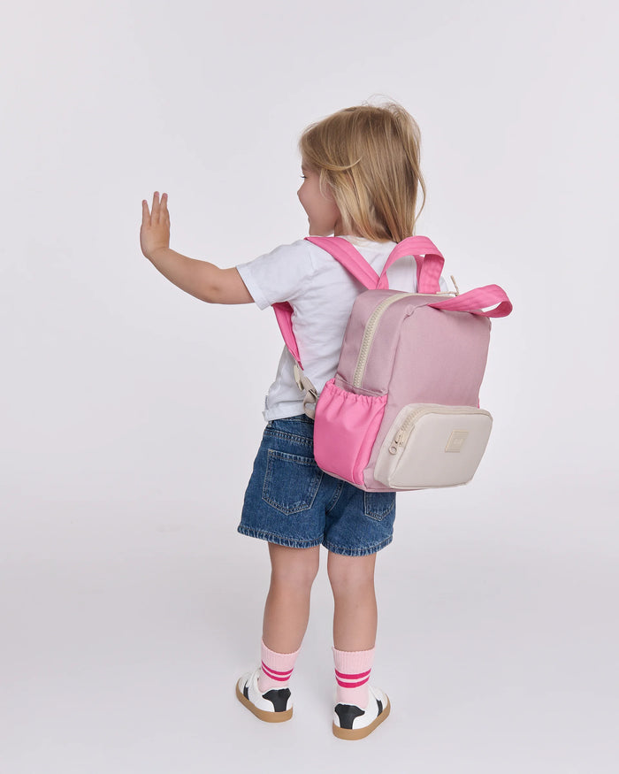 Child wearing a pink and beige backpack on a white background