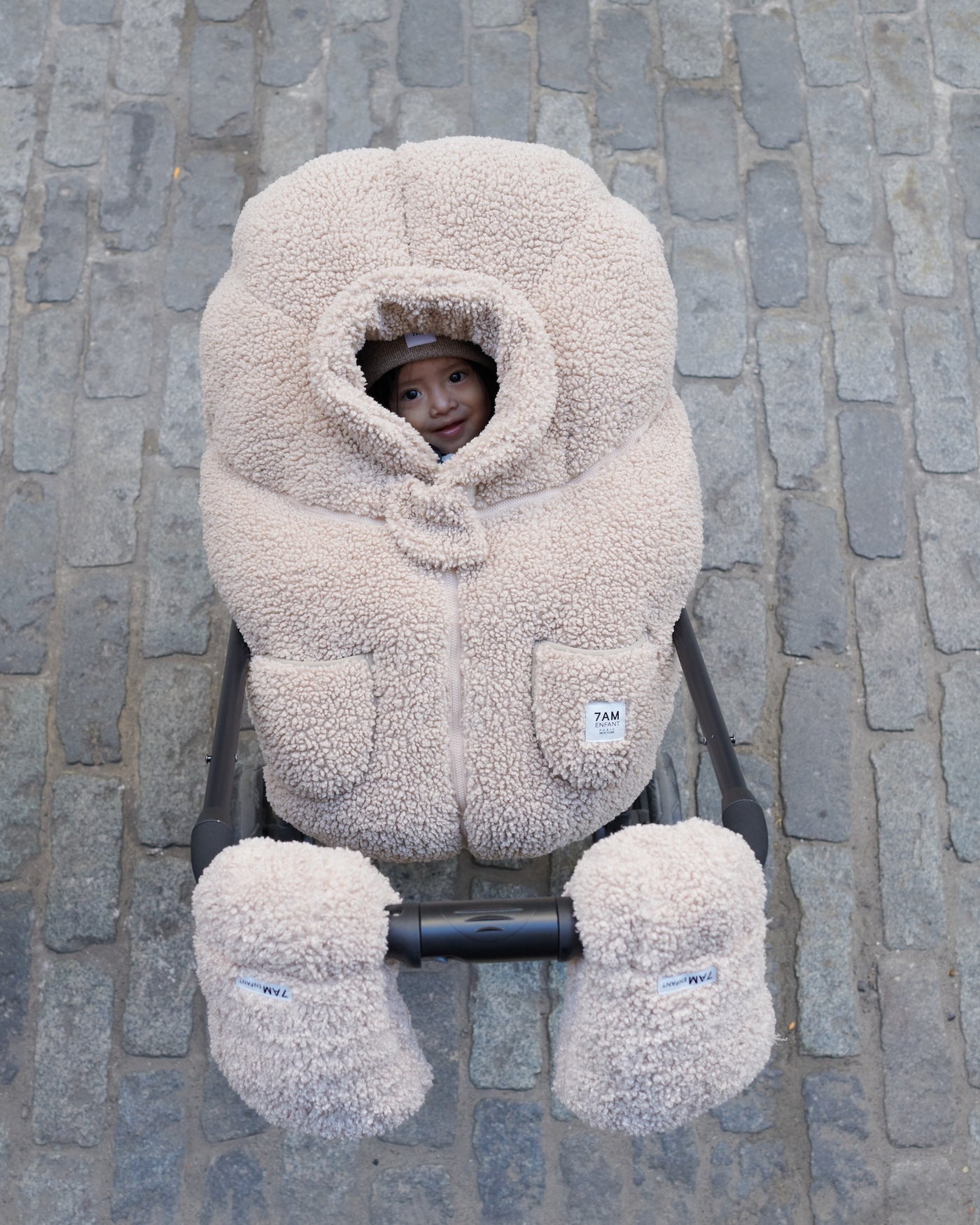 Child in a beige baby carrier on a stone pavement