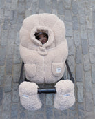 Child in a beige baby carrier on a stone pavement