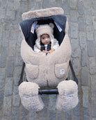 Child in a plush, beige stroller on a stone pavement