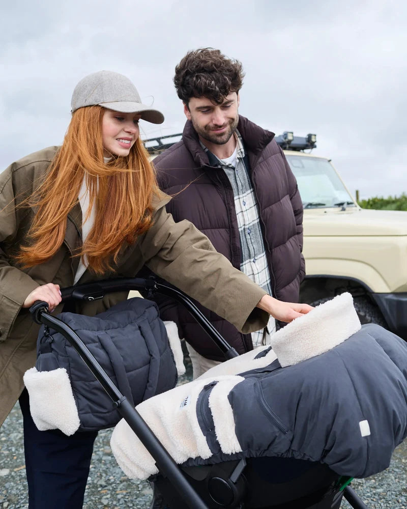A woman and a man outdoors next to a vehicle, with the woman pushing a stroller covered in a navy quilted baby liner with white sherpa lining.