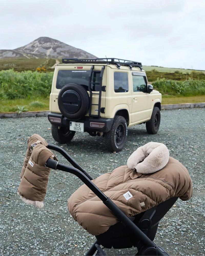 Stroller with the moss brown Helsinki Car Seat Cocoon by 7AM Enfant parked outdoors with an off-road vehicle and mountain landscape in the background.