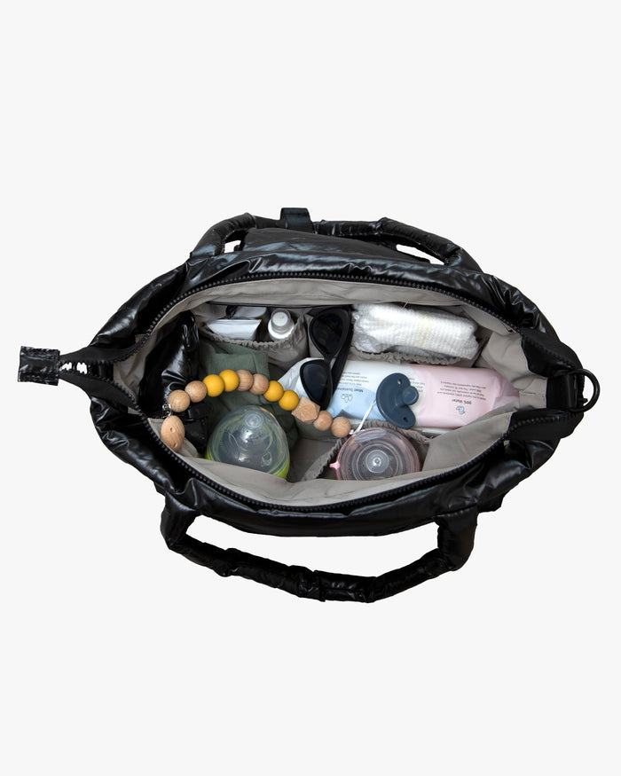 Black diaper bag open with baby items on a white background