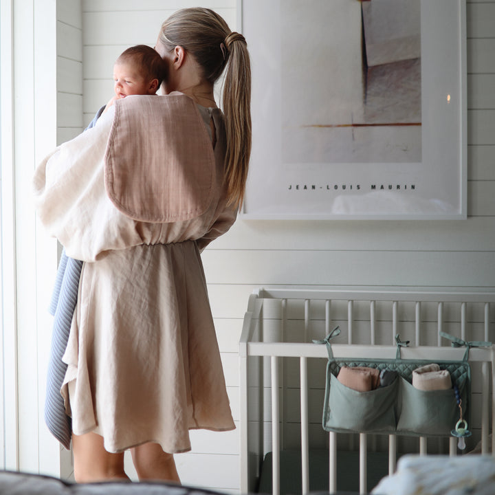 Woman holding a baby in a room with a crib and wall art.