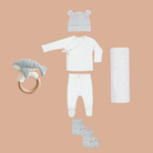 Baby clothing and accessories including a hat, onesie, pants, booties, and a ring on a beige background.