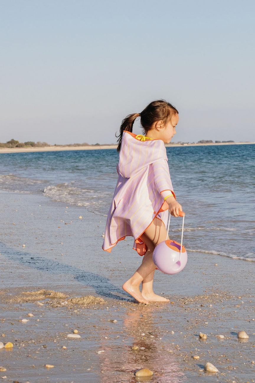 Child in a pink outfit walking on a beach with a sand bucket.