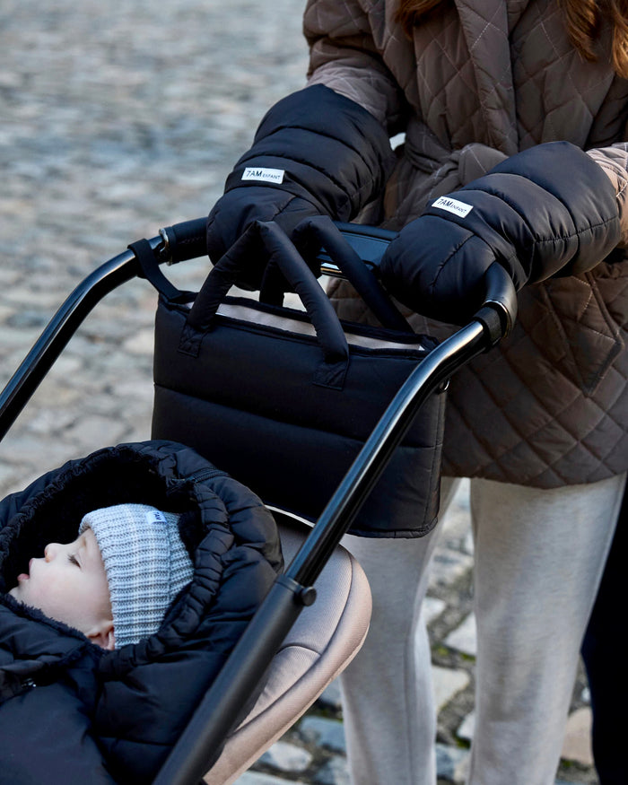 Person pushing a stroller with a baby, wearing insulated gloves and a coat.