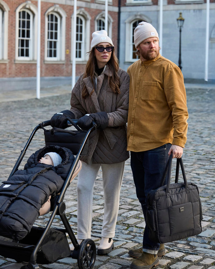 Two adults with a child in a stroller on a cobblestone street.