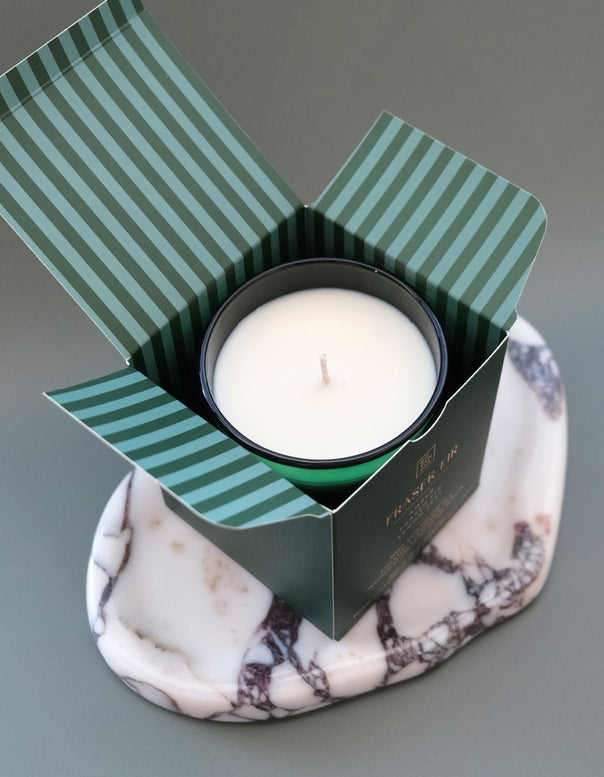 White candle in a black container with green striped lid on a marble coaster