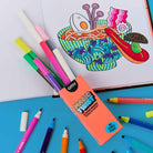 Colorful markers with an open coloring book featuring a bowl of noodles on a blue surface.