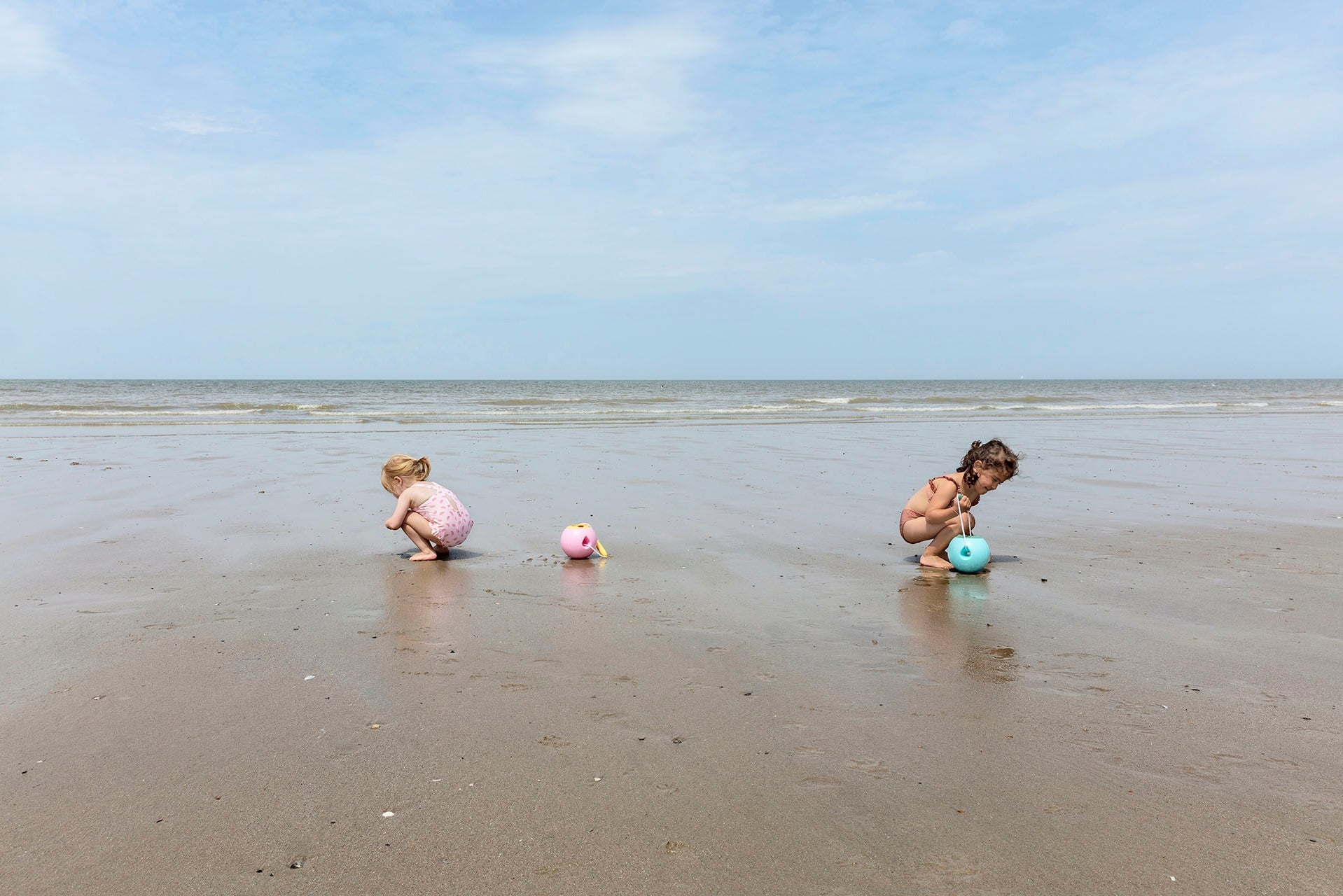 Two children playing on a sandy beach with toys.
