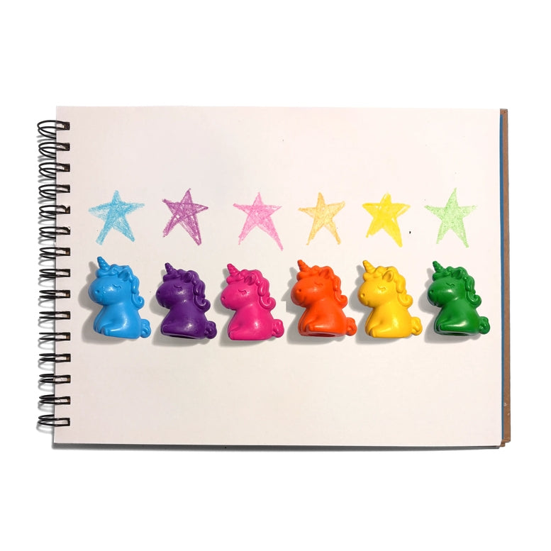 Six colorful unicorn-shaped crayons in blue, purple, pink, orange, yellow, and green are lined up on a white spiral notebook page below matching colored star crayons.
