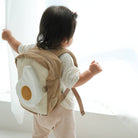 Child wearing a backpack with an egg design in a bright room