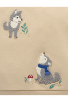 Close-up of a beige textile with two embroidered wolf motifs, one standing and one sitting with a blue scarf, plus small green leaves and a red-and-white mushroom detail.