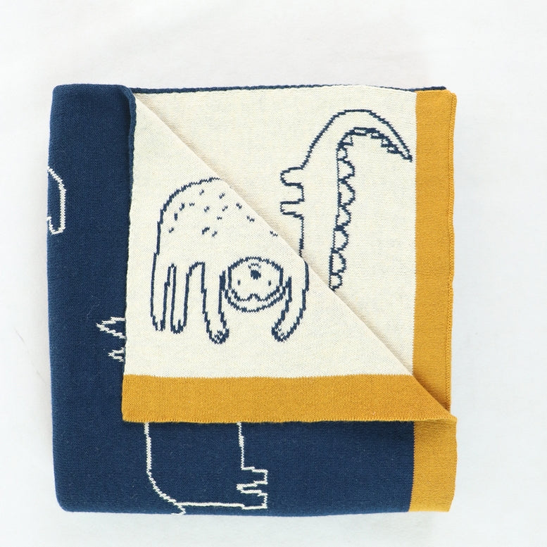 A folded knit blanket featuring a cream center with blue line-art illustrations of a creature and a tentacle, bordered by navy blue and mustard yellow sections on a white background.