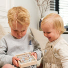 Two children playing with a wooden puzzle on a couch in a living room.