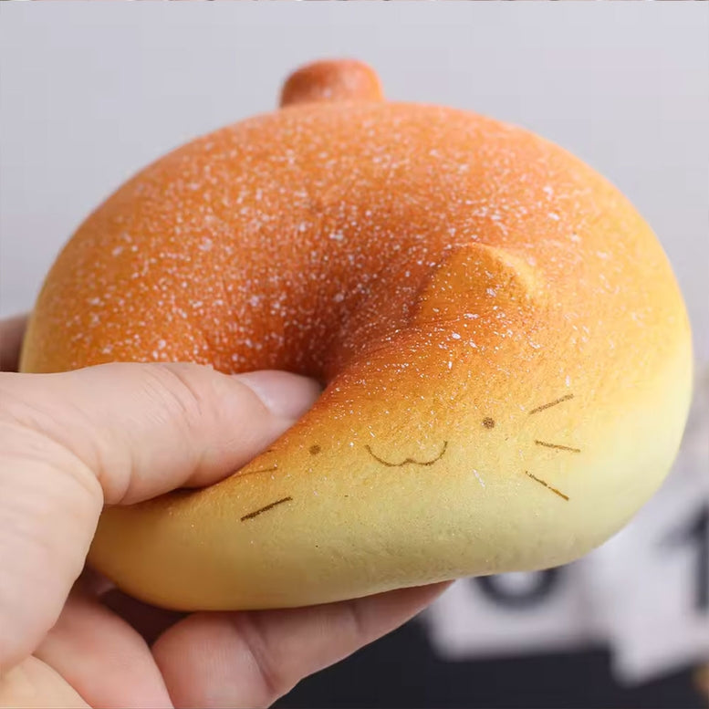 A hand holding a cat-shaped squishy toy made to look like a baked bun, with a smiling face drawn on the front.