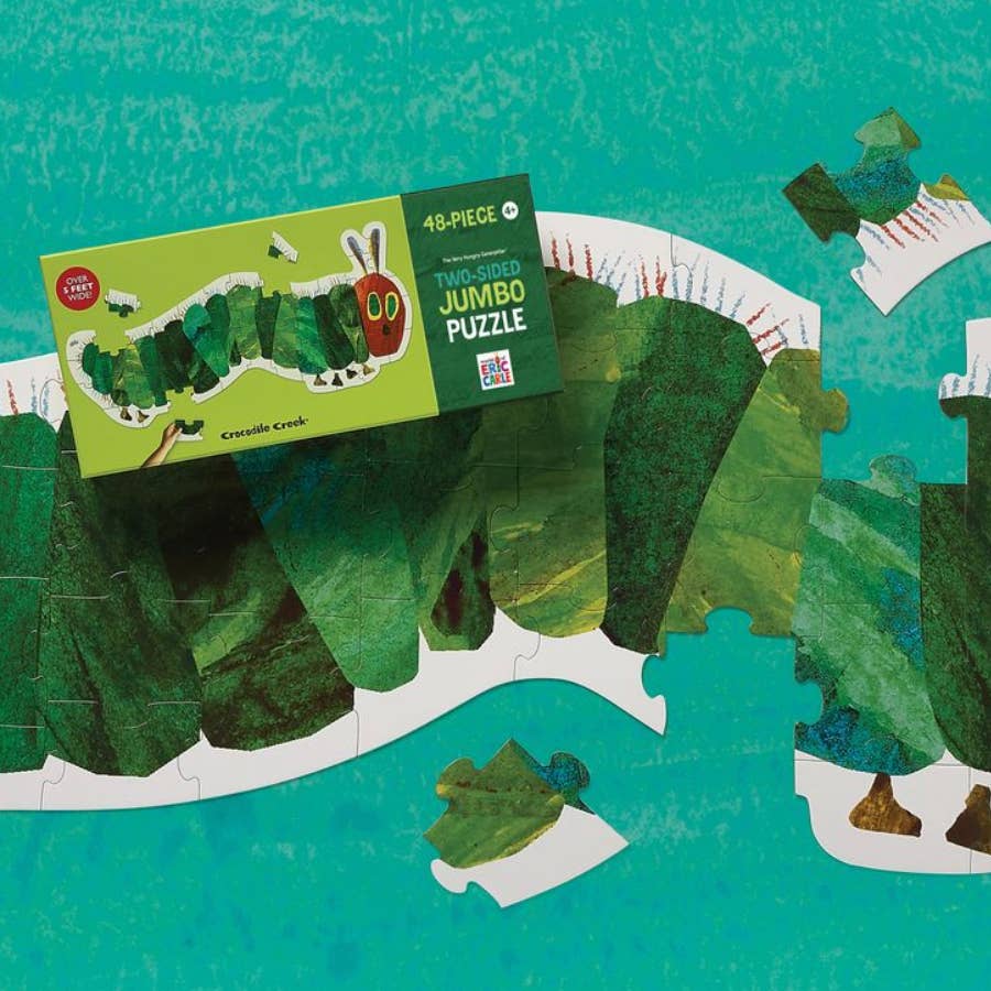 The Crissis Green Jumbo Puzzle box placed on top of a partially assembled green leaf collage puzzle, with a few loose puzzle pieces scattered around on a turquoise textured background.