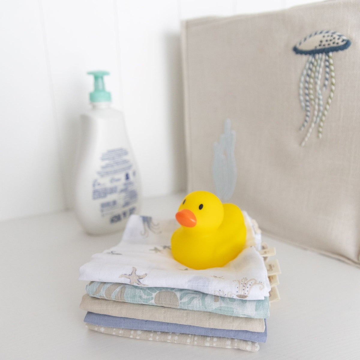 Stack of baby blankets with a yellow rubber duck on top, against a neutral background.