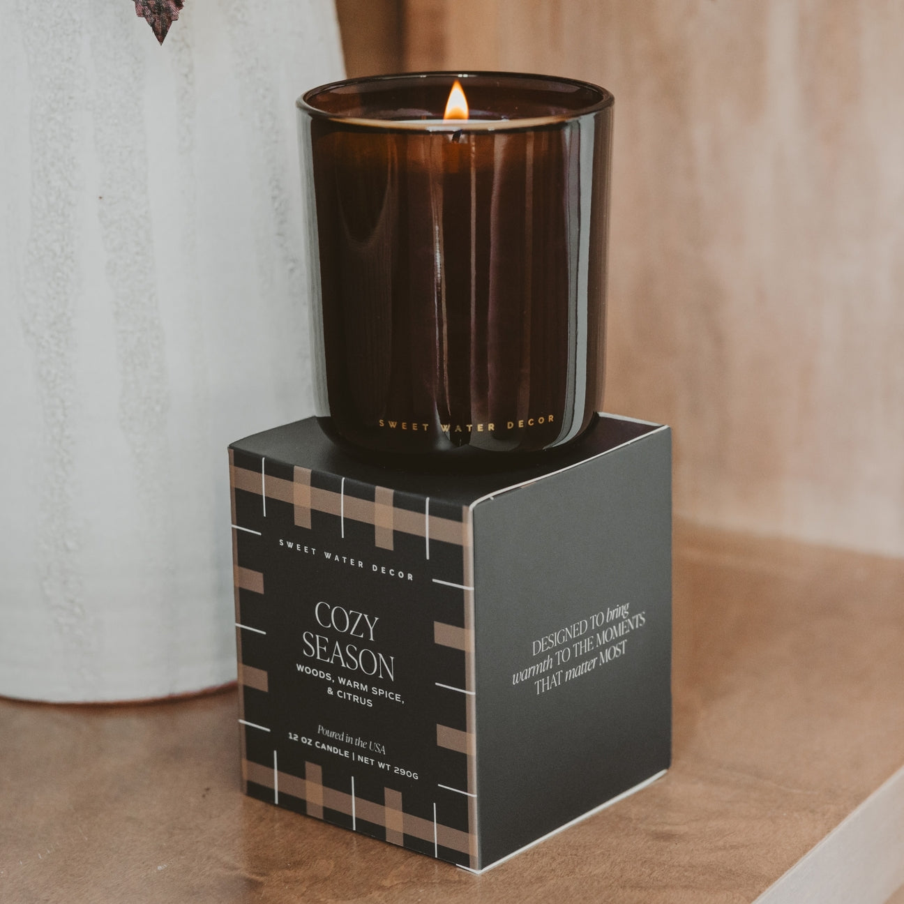 Candle in a decorative box labeled 'Cozy Season' on a wooden surface.
