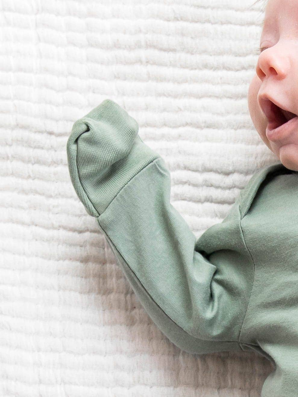 Baby wearing a light green outfit on a textured white blanket