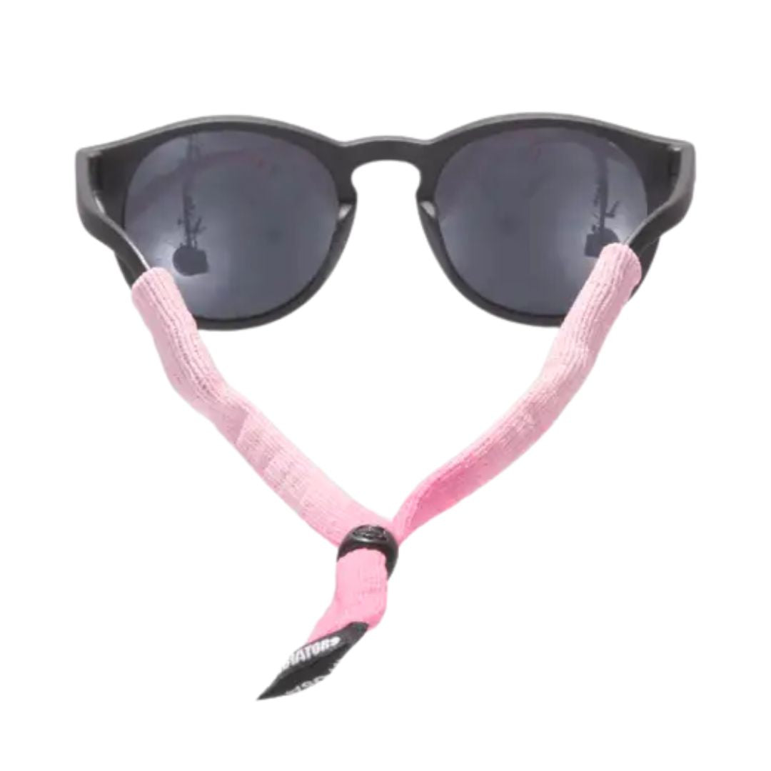 Black sunglasses with dark gray lenses and a pink textured fabric chin strap, shown against a plain white background.